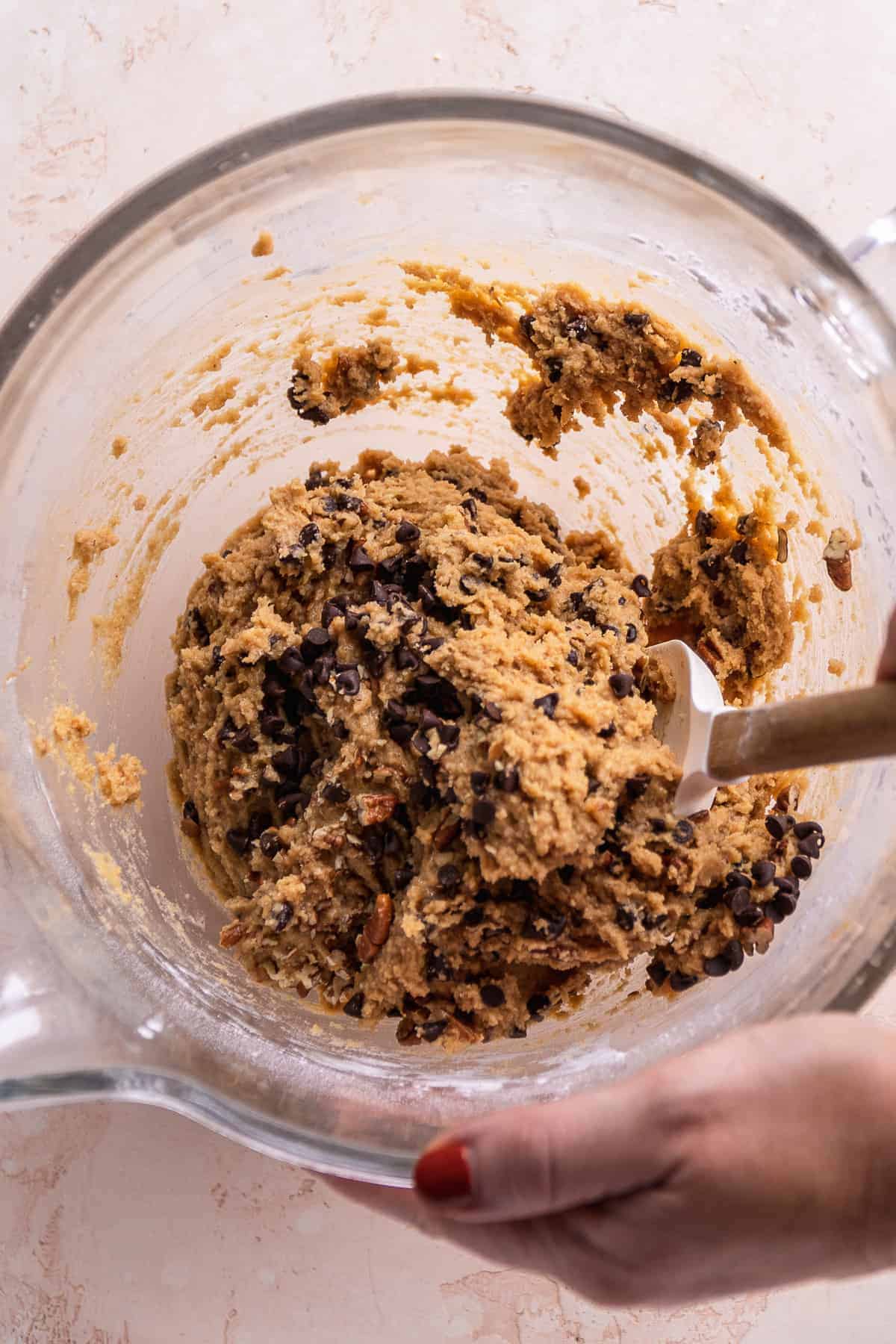 Person mixing chocolate chips and nuts into scone batter.