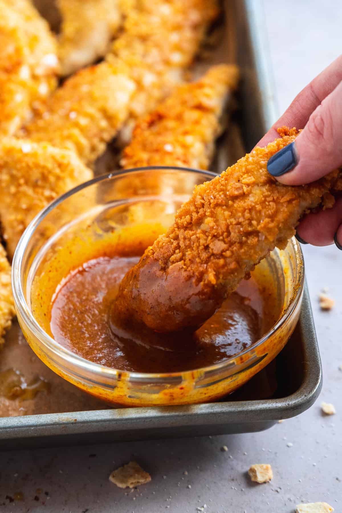 Person dipping chicken tender in a bowl of sauce.