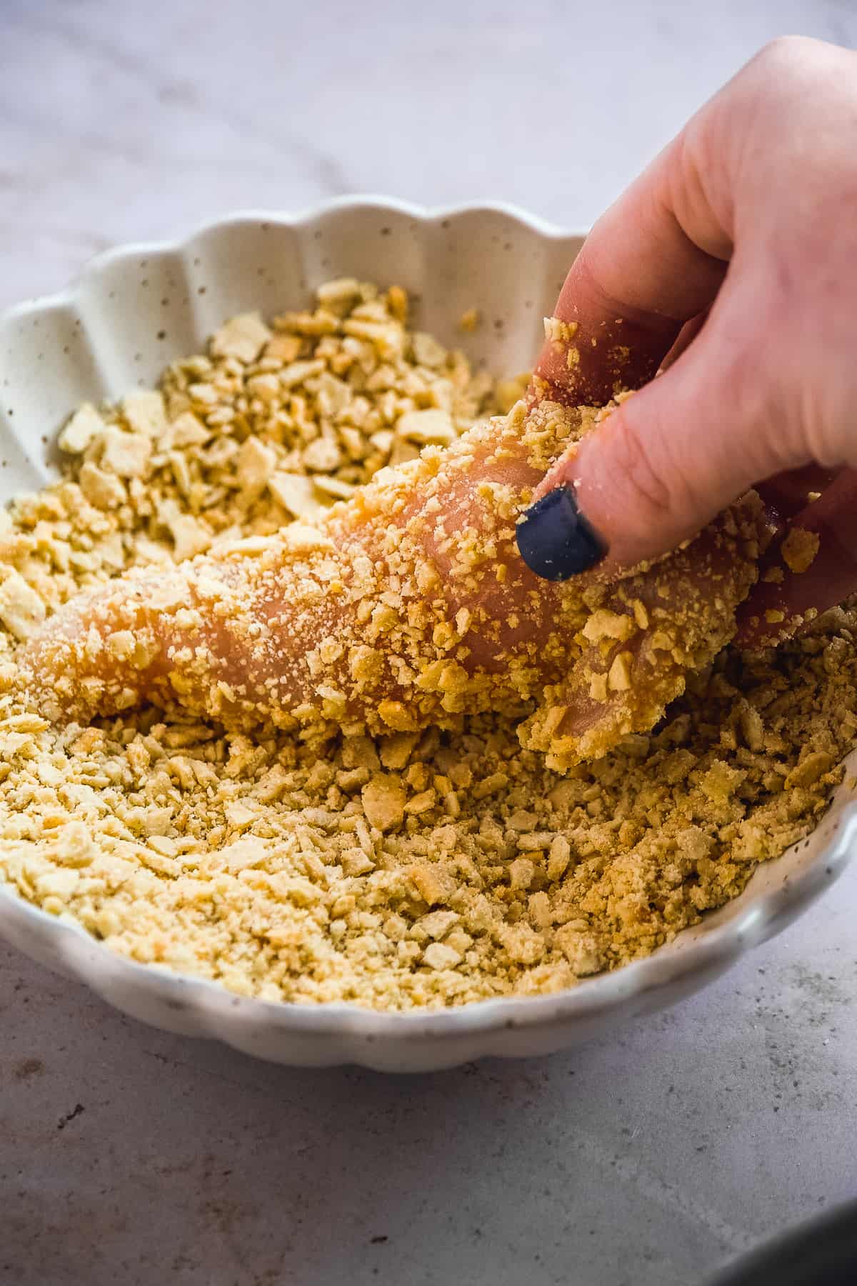 Person coating chicken tender in crushed crackers.