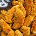 Breaded chicken tenders scattered on a baking pan.