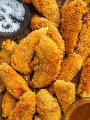 Breaded chicken tenders scattered on a baking pan.