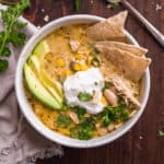 Bowl of chicken chili with chips and avocados inside on a wooden backdrop.