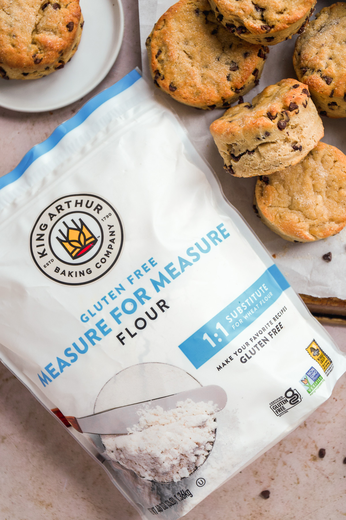Bag of gluten free flour laying next to chocolate chip biscuits.