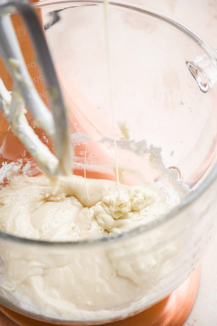 Melted white chocolate being poured into a glass bowl with frosting.