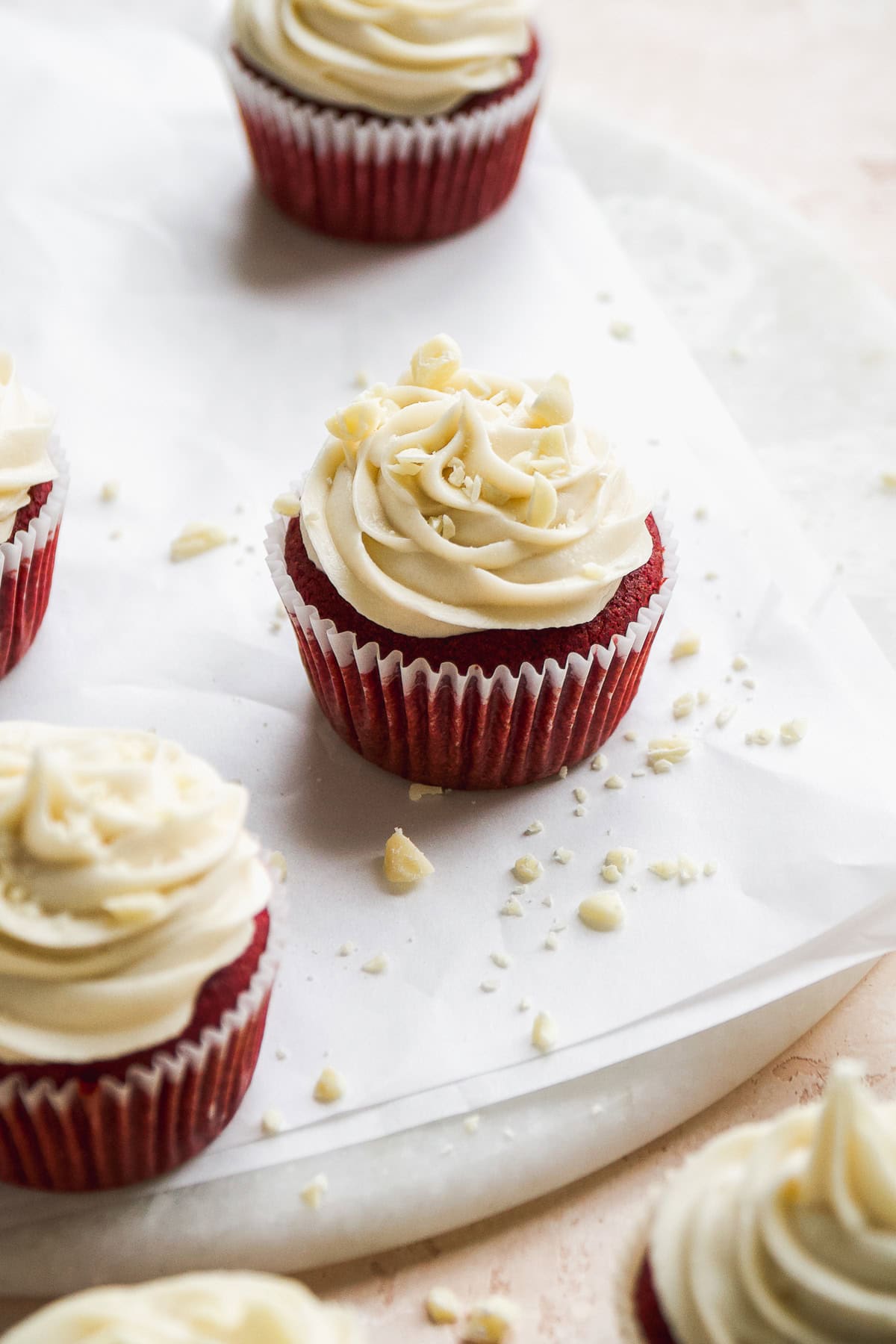 Red velvet cupcakes with cream cheese frosting on top on white parchment paper.