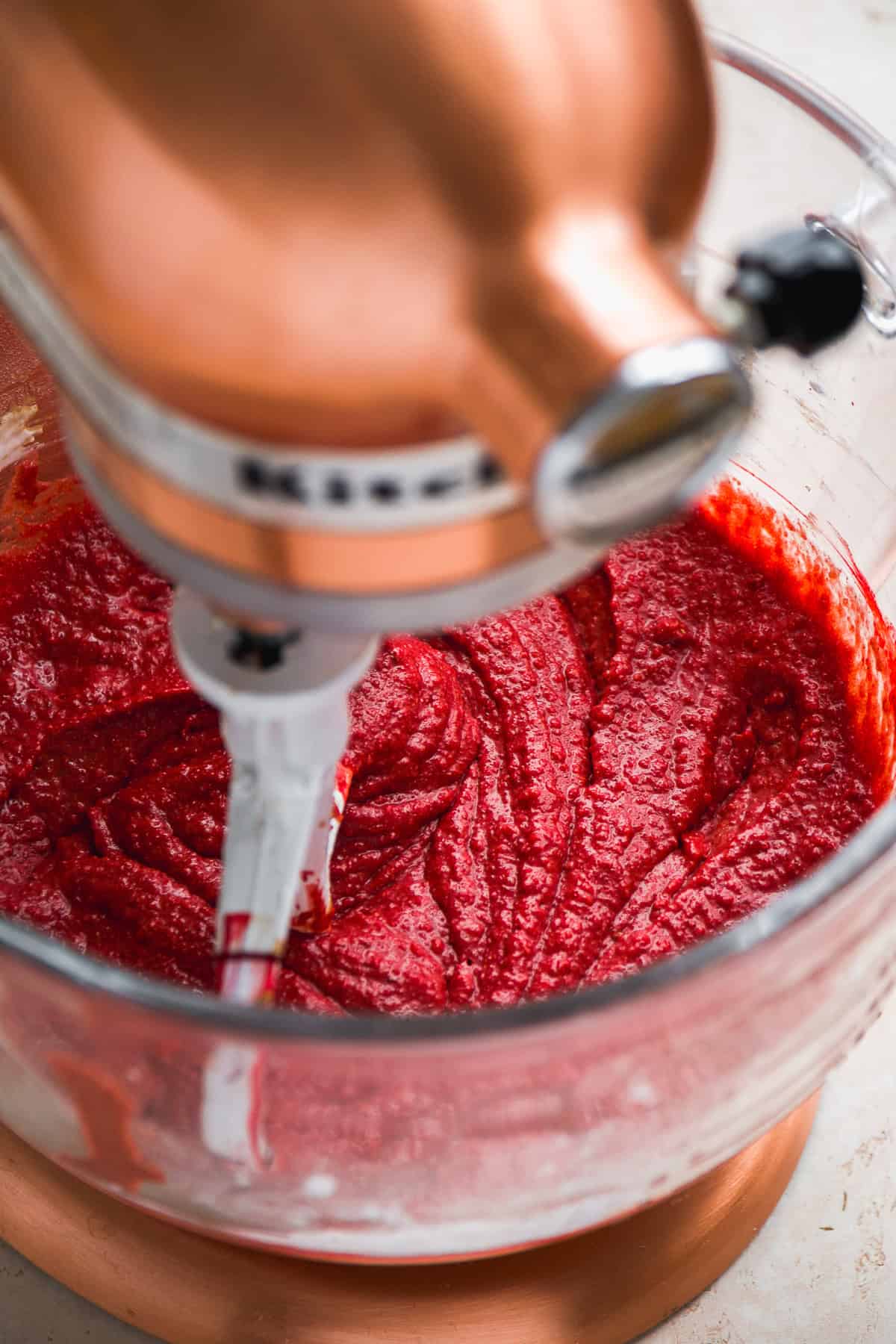 Red velvet cupcake batter in a glass mixer being mixed.