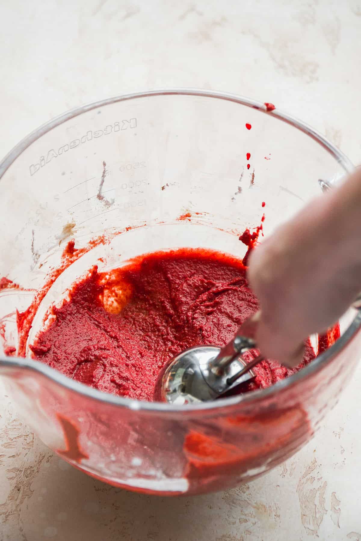 Person scooping red velvet cupcake batter with a scoop.