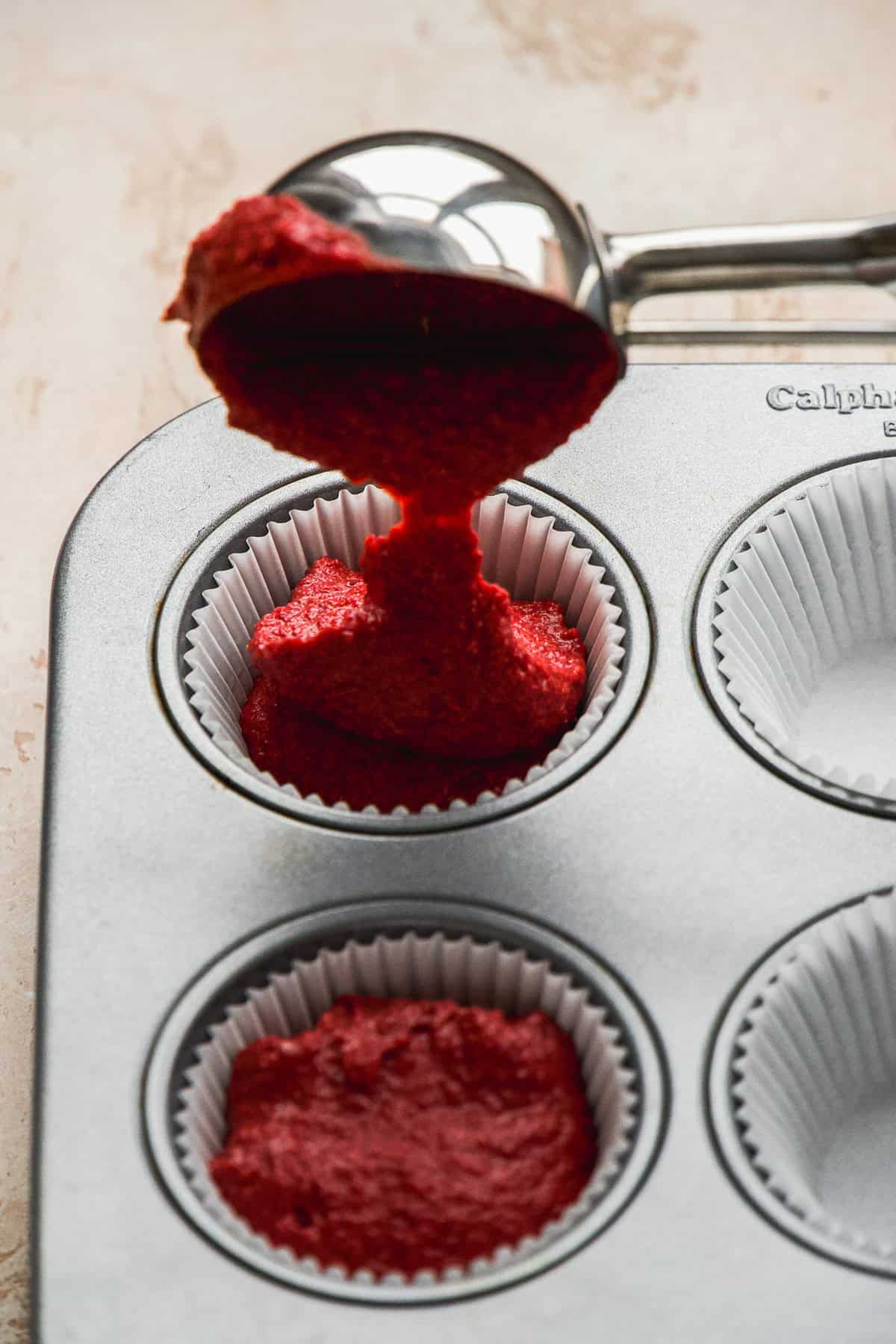 Person pouring red velvet cupcake batter into muffin tin.