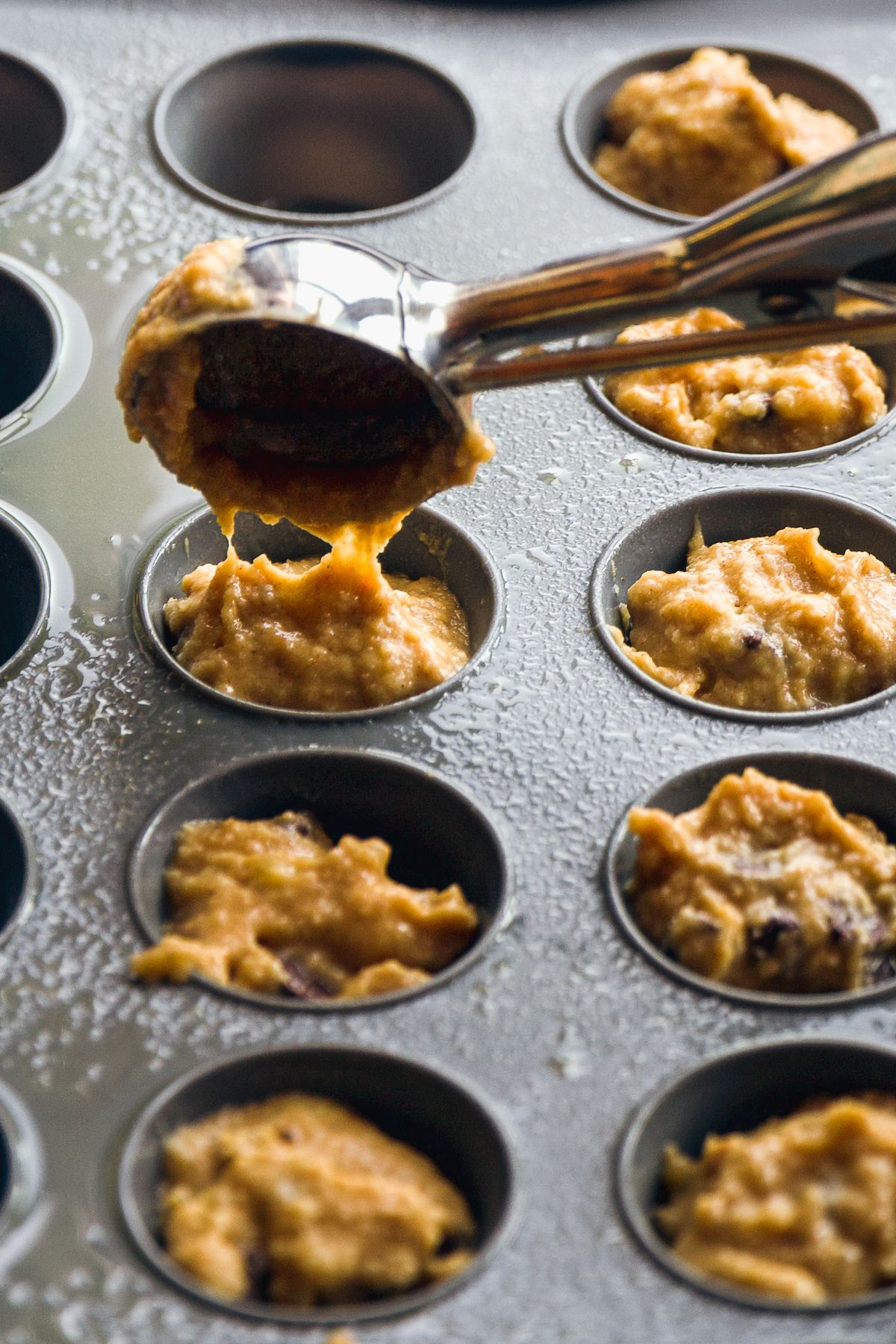 Muffin batter being poured into a mini muffin pan.