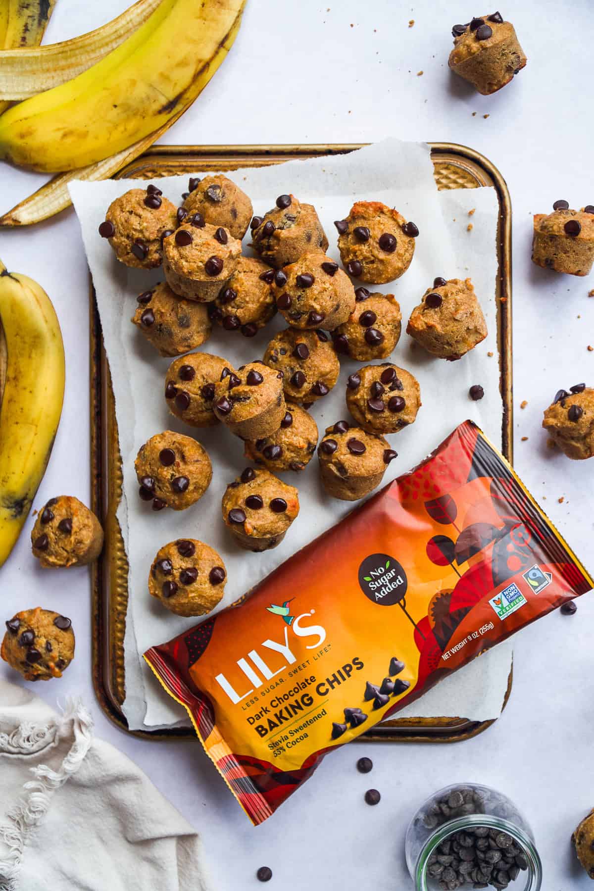 Mini muffins scattered on a baking pan with a bag of chocolate chips.