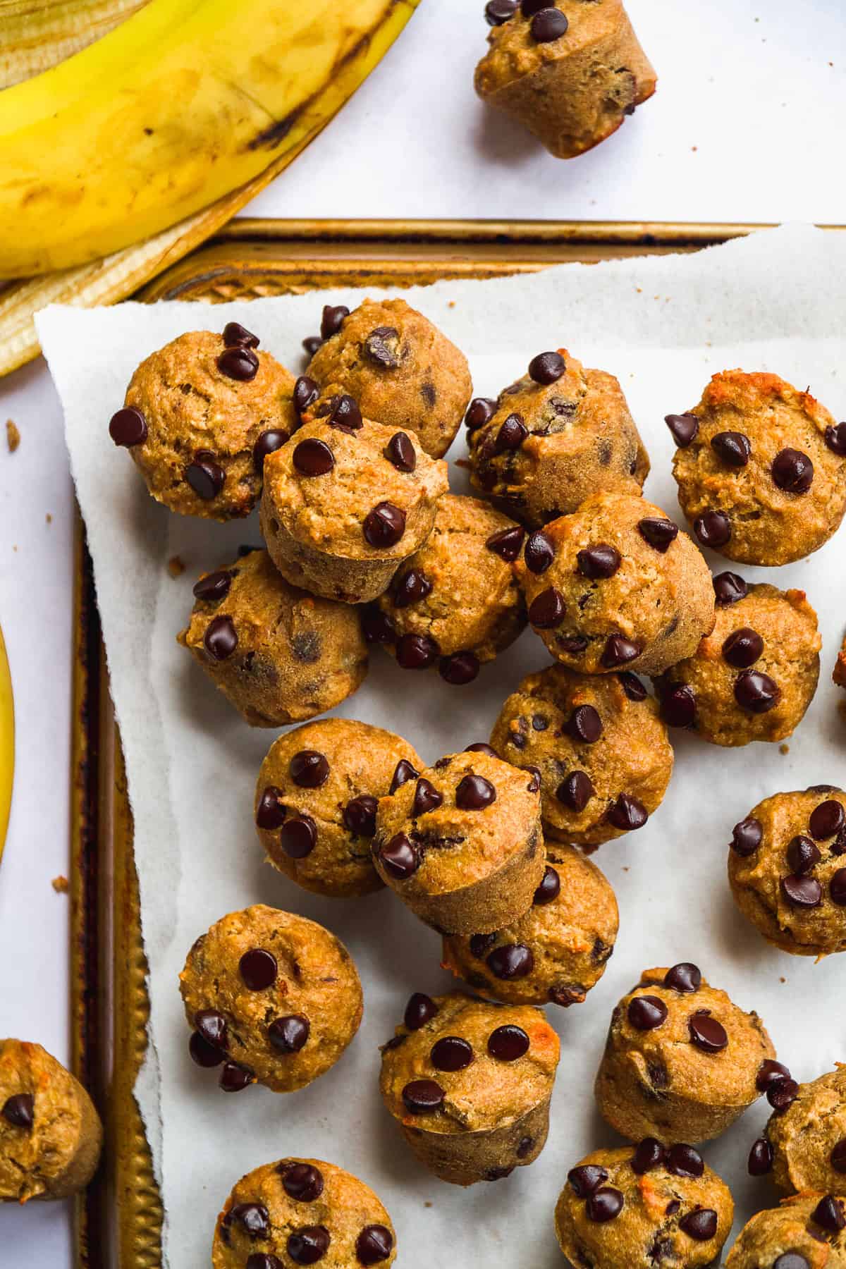 Mini gluten free banana muffins scattered on parchment paper.