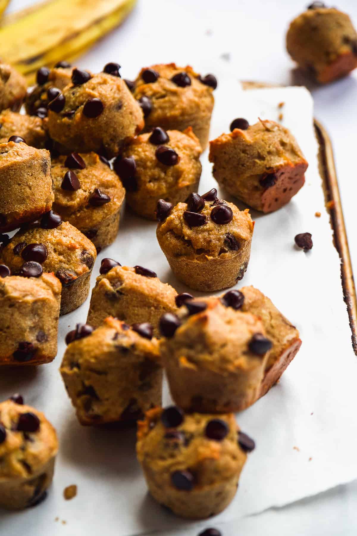 Mini muffins with chocolate chips scattered on parchment paper.