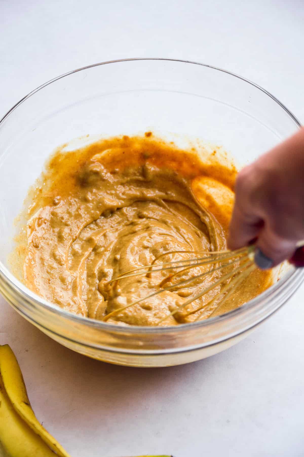 Person whisking a tan mixture in a glass mixing bowl.