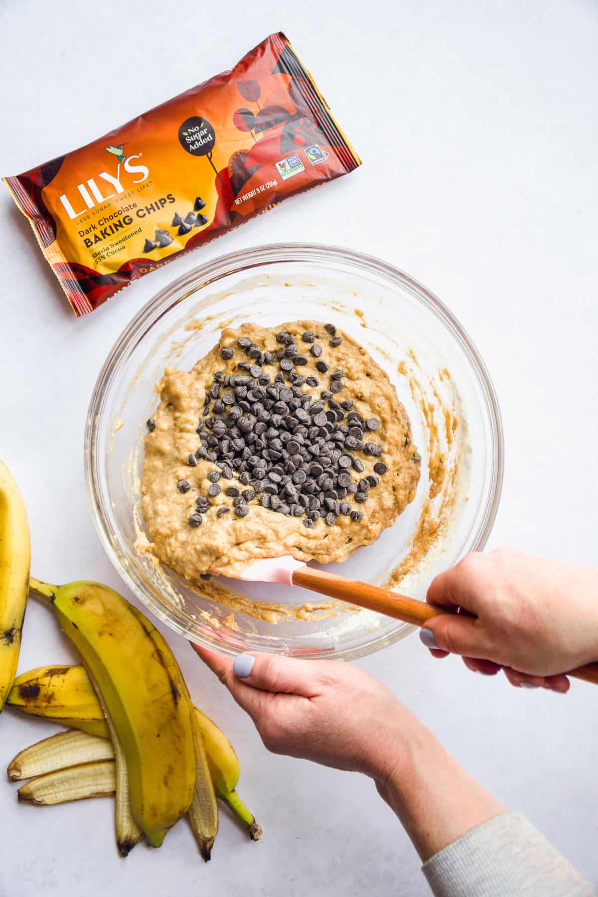 Person folding chocolate chips into banana muffin batter.