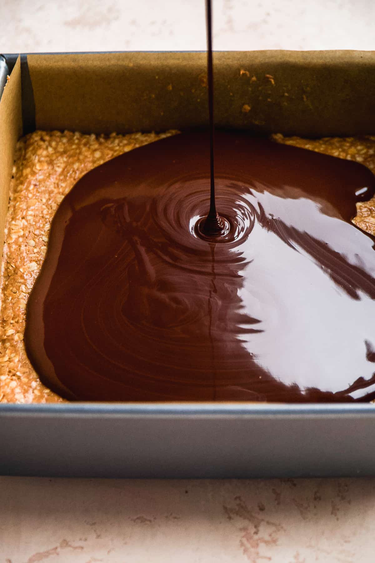 Chocolate being poured over a layer of peanut butter oats.