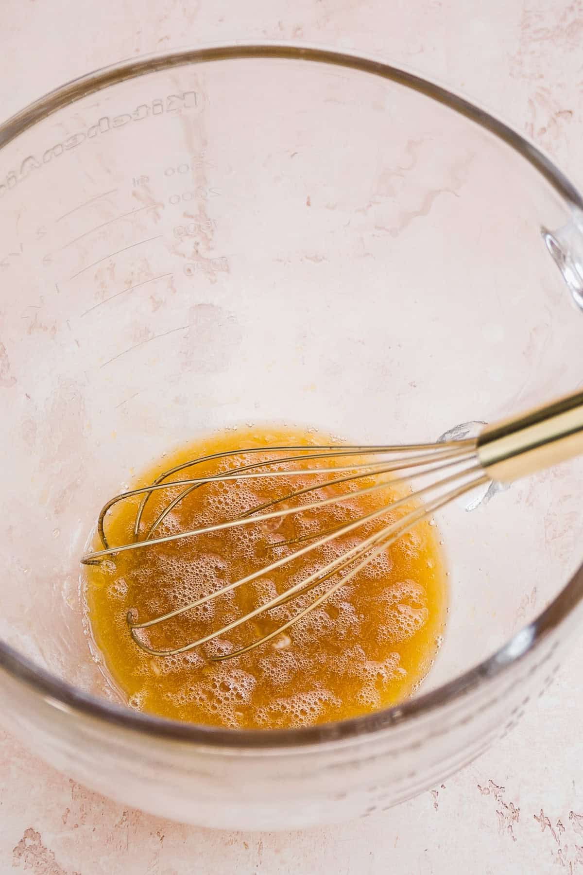 Liquid cookie ingredients in a mixing bowl with a whisk.