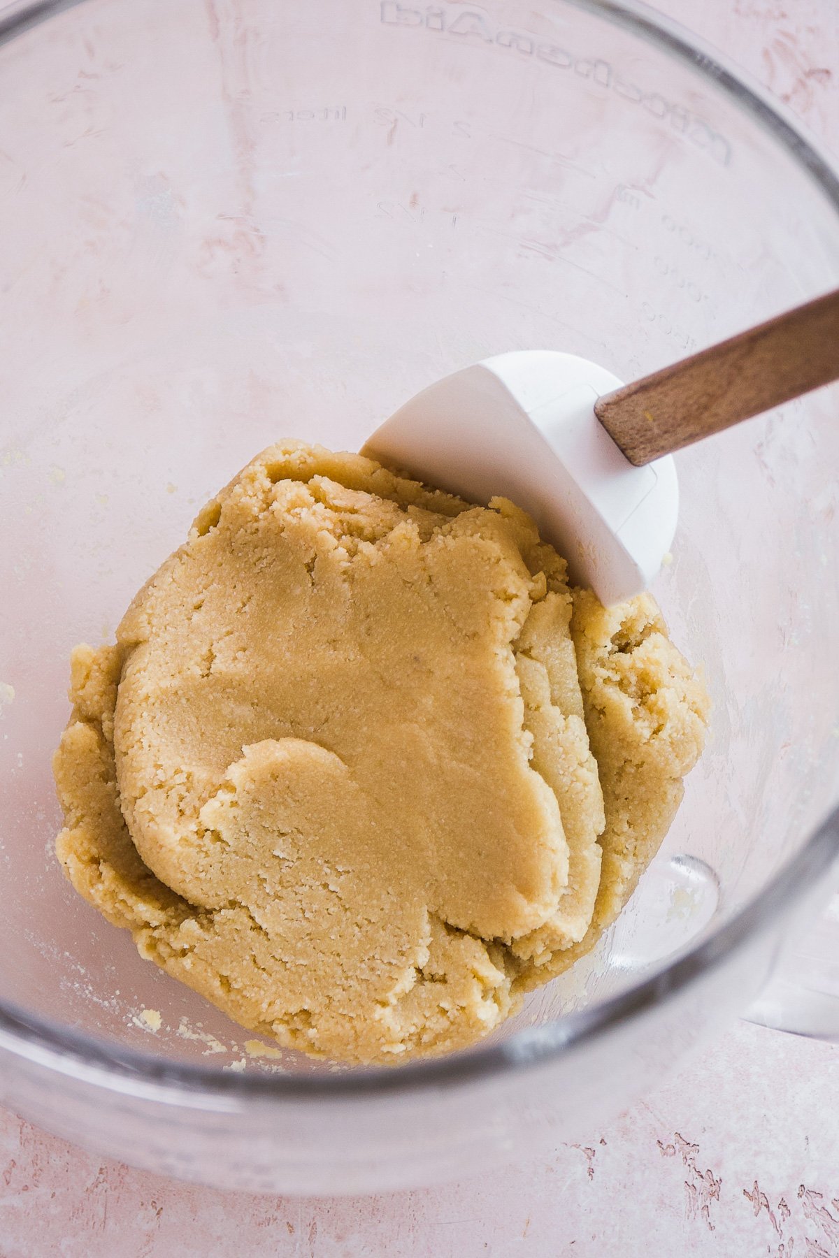 Sugar cookie dough in a glass mixing bowl with a rubber spatula inside.