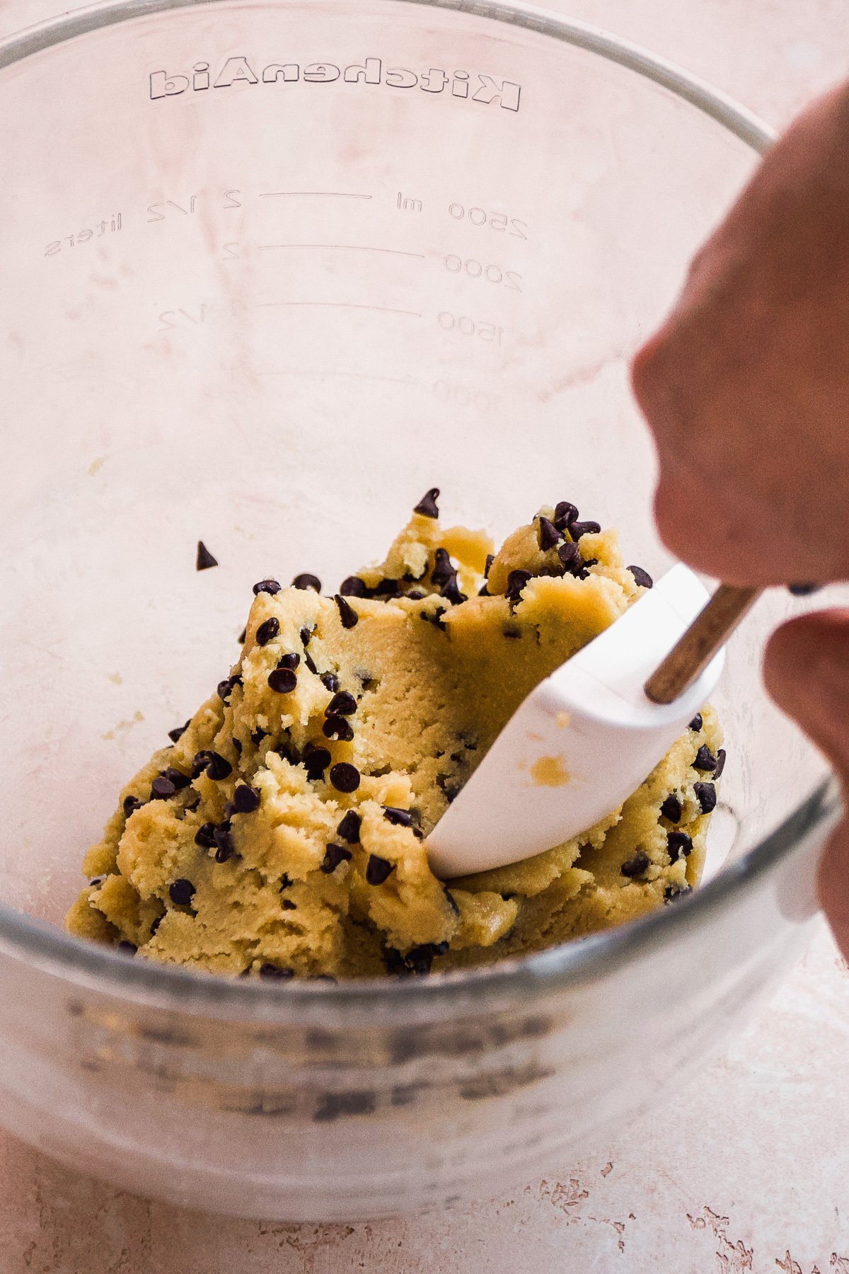 Person mixing chocolate chips into sugar cookie dough.
