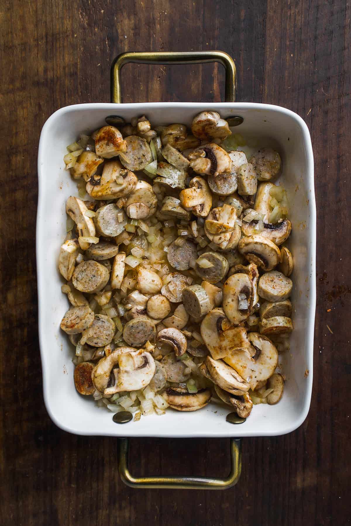 Baking dish with sausage and mushrooms mixed with spices.