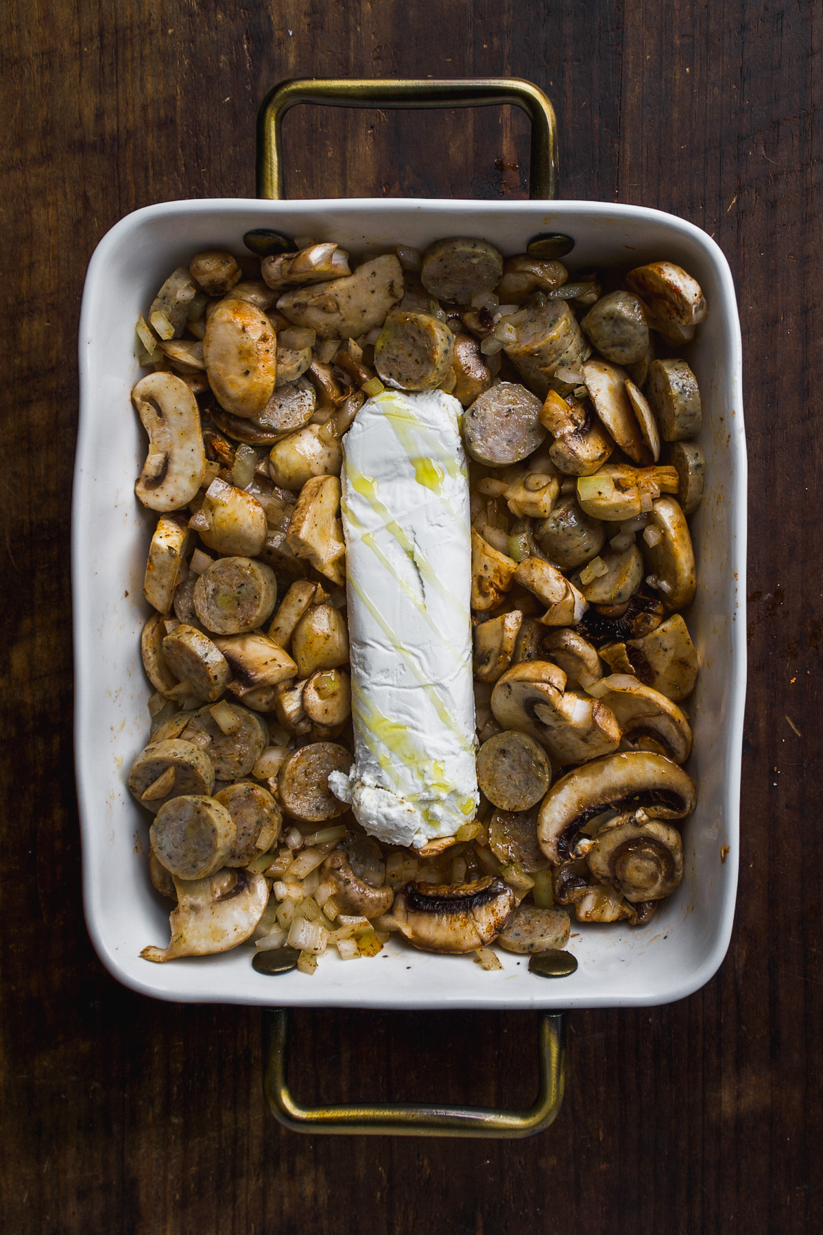 Goat cheese log in a baking dish with mushrooms and sausage.