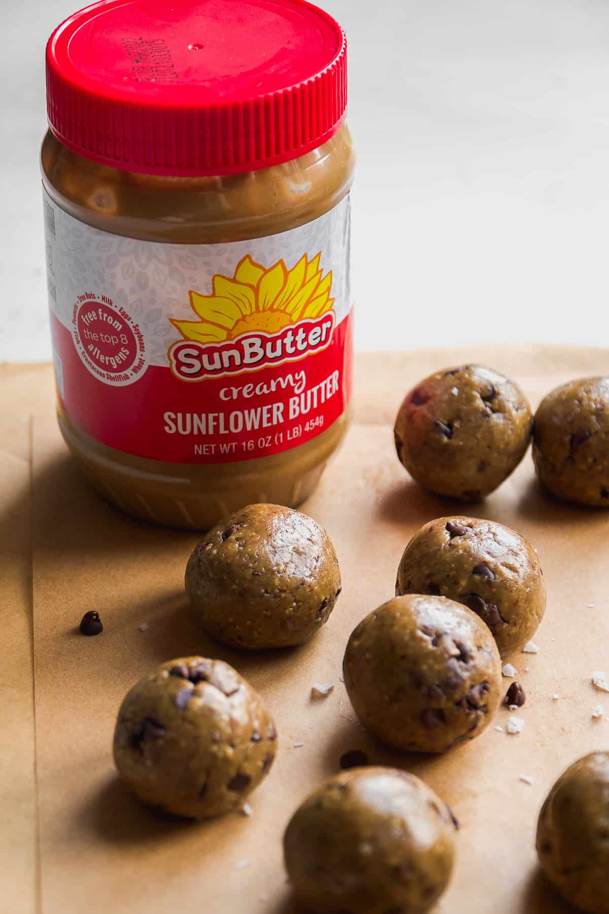 Cookie dough balls on parchment paper with a jar of sunflower butter with a red lid.