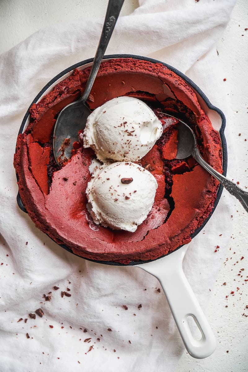 Red velvet cookies skillet with ice cream on top on a white surface.