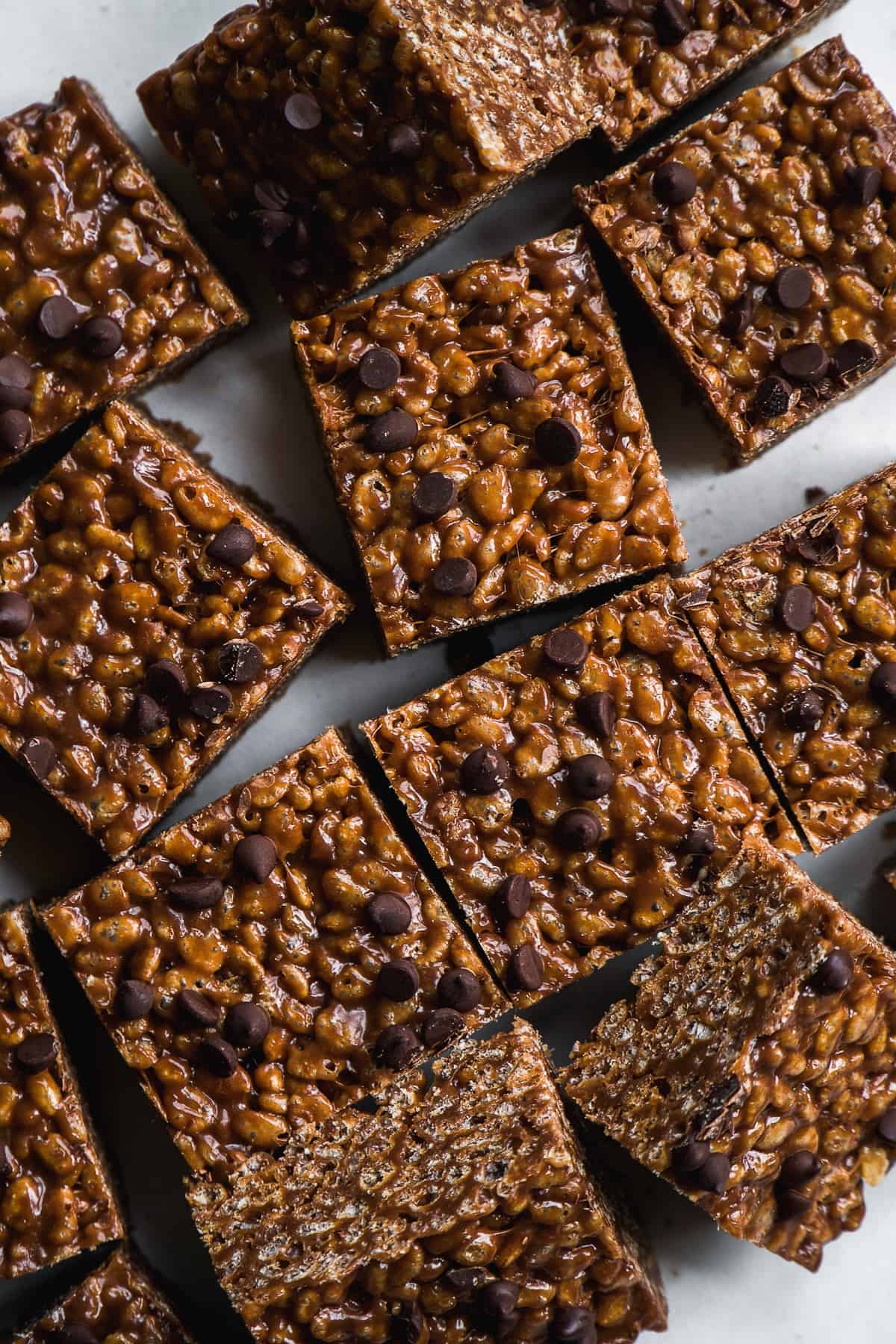 Chocolate rice krispies cut into squares scattered on a white surface.