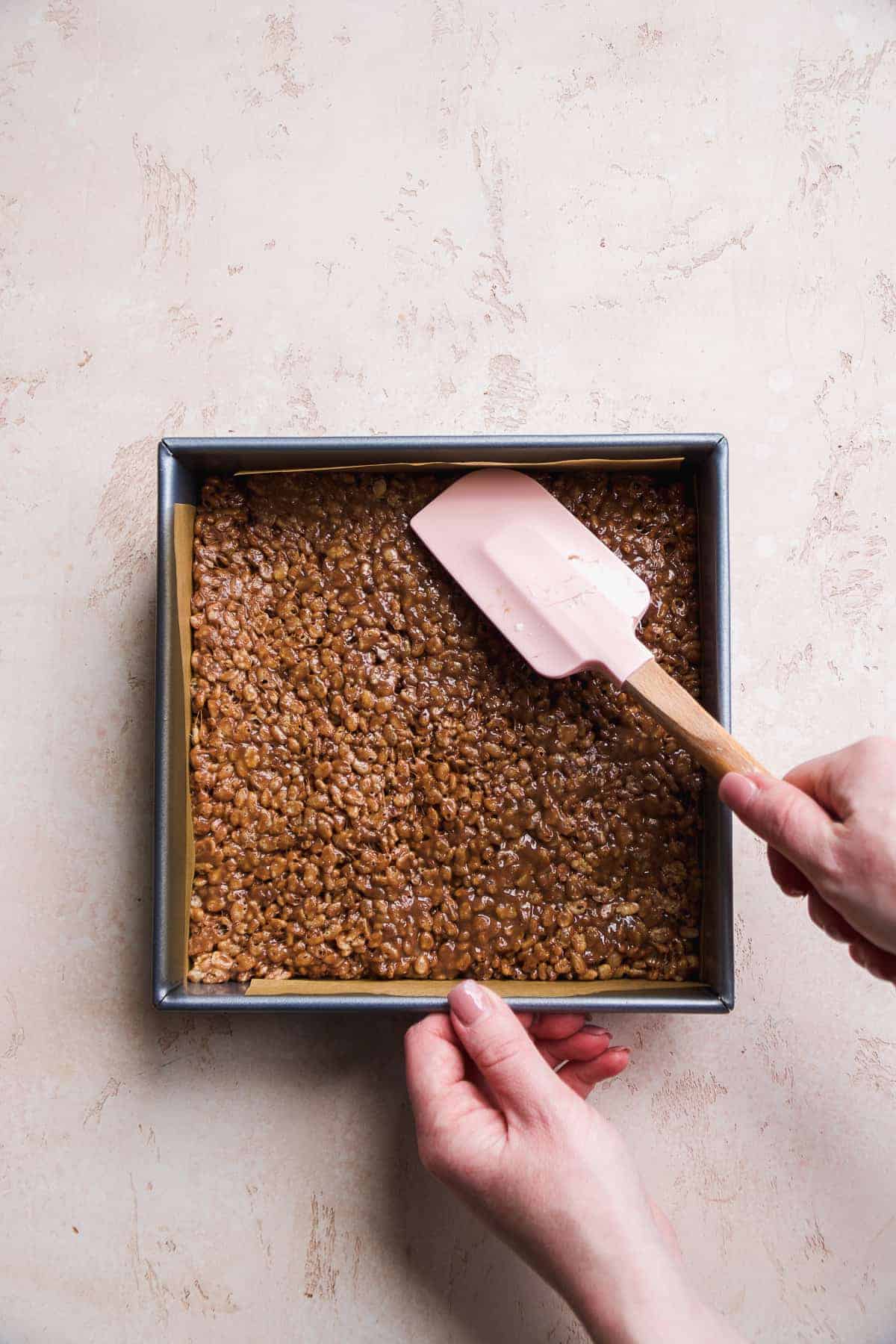 Person pressing chocolate rice krispies into a square pan.