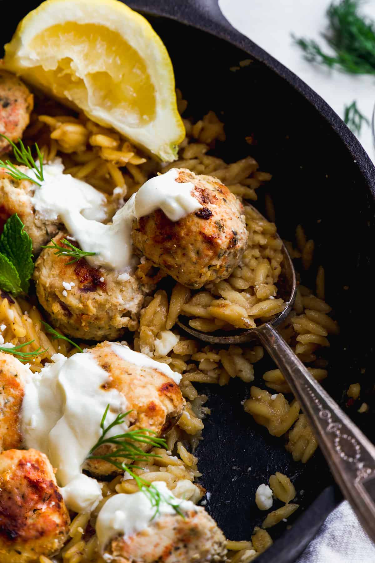 Orzo greek chicken meatball skillet with herbs and a spoon resting inside.