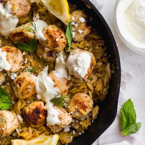 Skillet with greek chicken meatballs and orzo and garnished with greenery