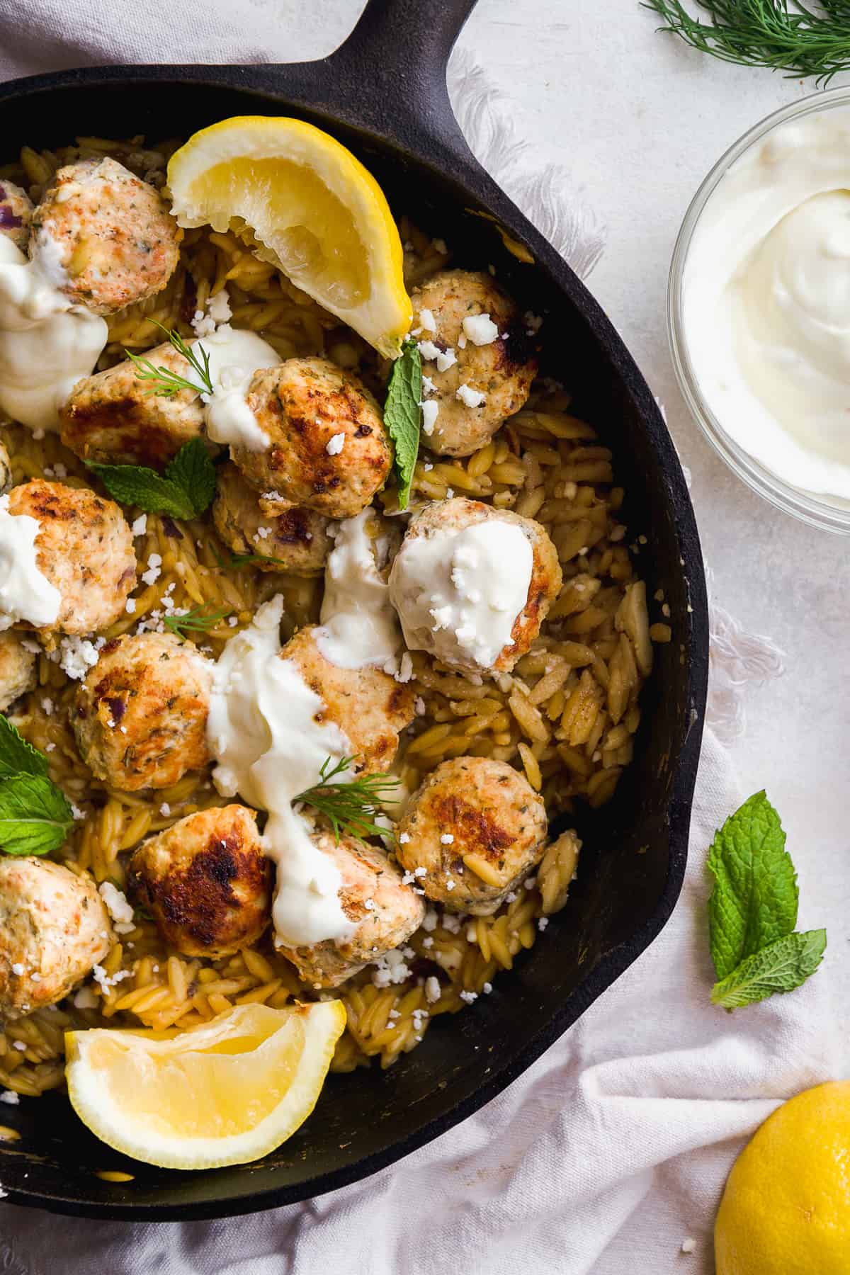 Overhead view of a black skillet with orzo and greek chicken meatballs.
