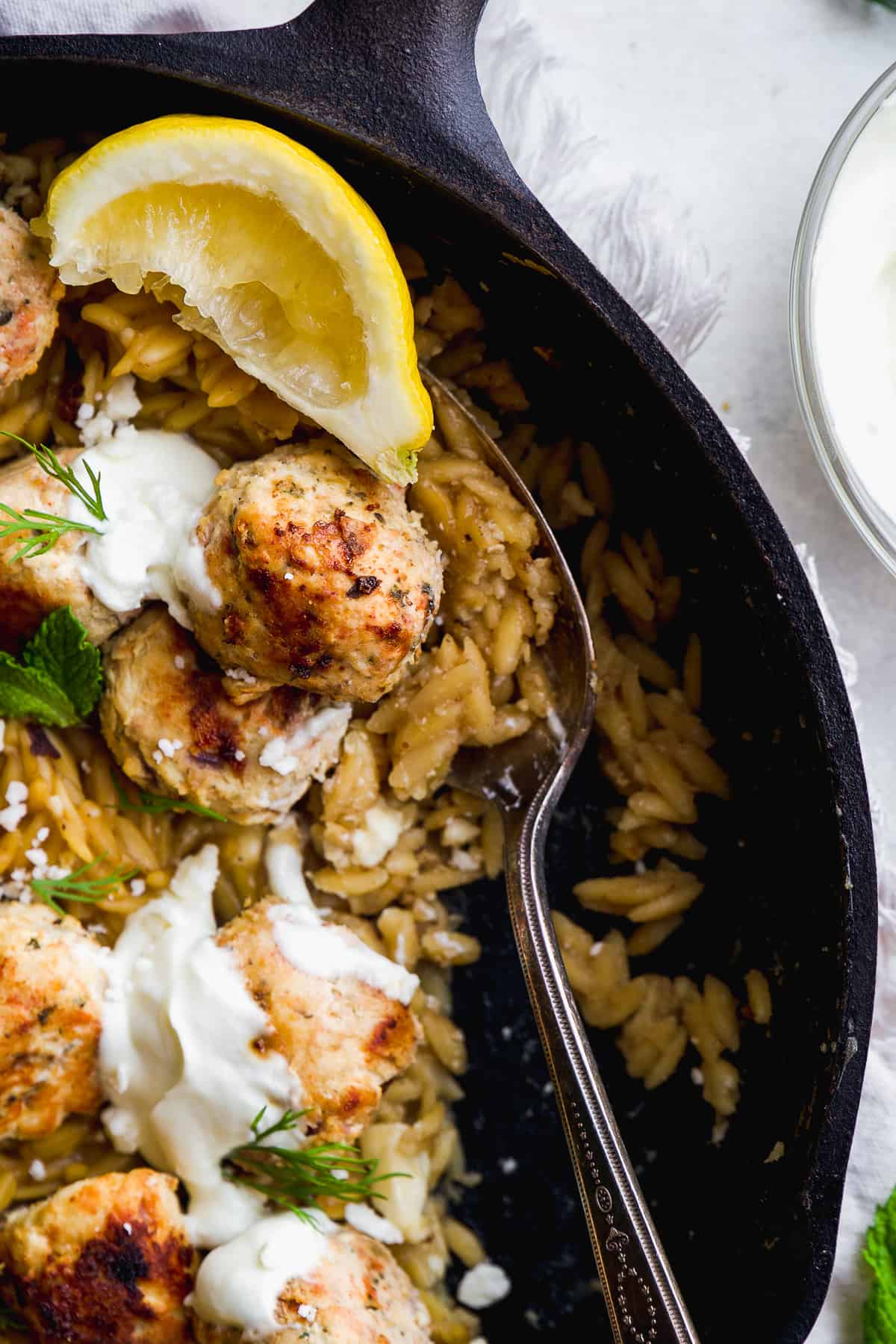 Greek meatballs and orzo in a skillet with herbs and a serving spoon.