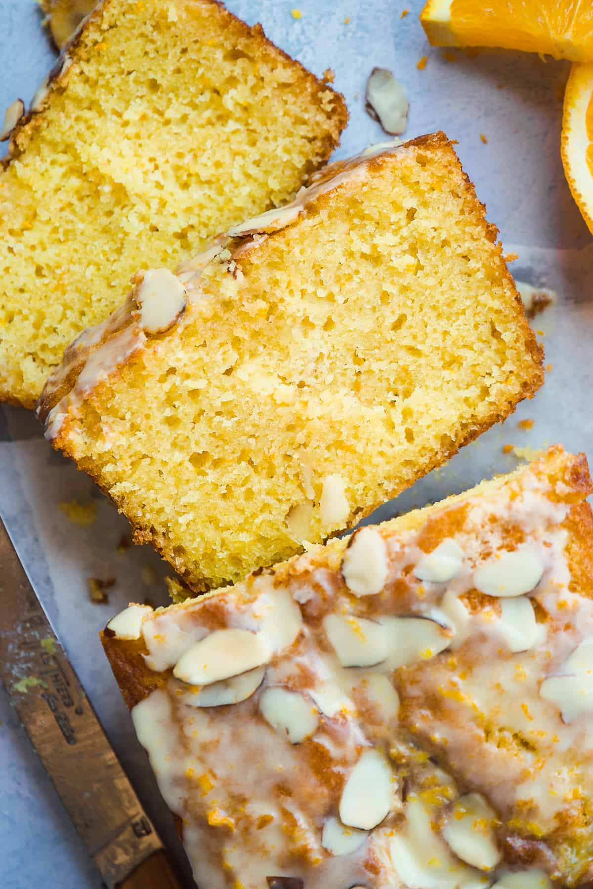 Slices of orange pound cake scattered on a blue surface with almonds on top.