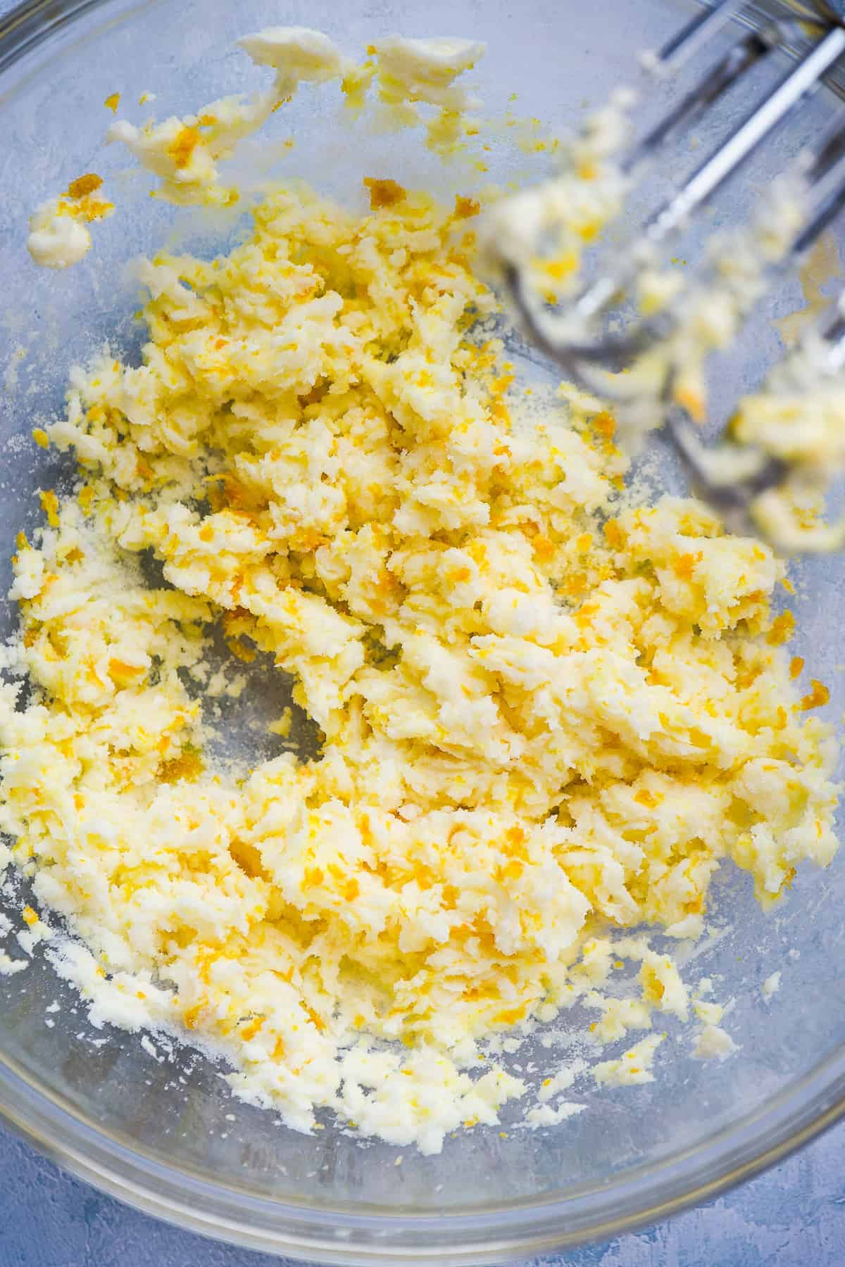 Clear mixing bowl with butter being creamed together with orange zest.