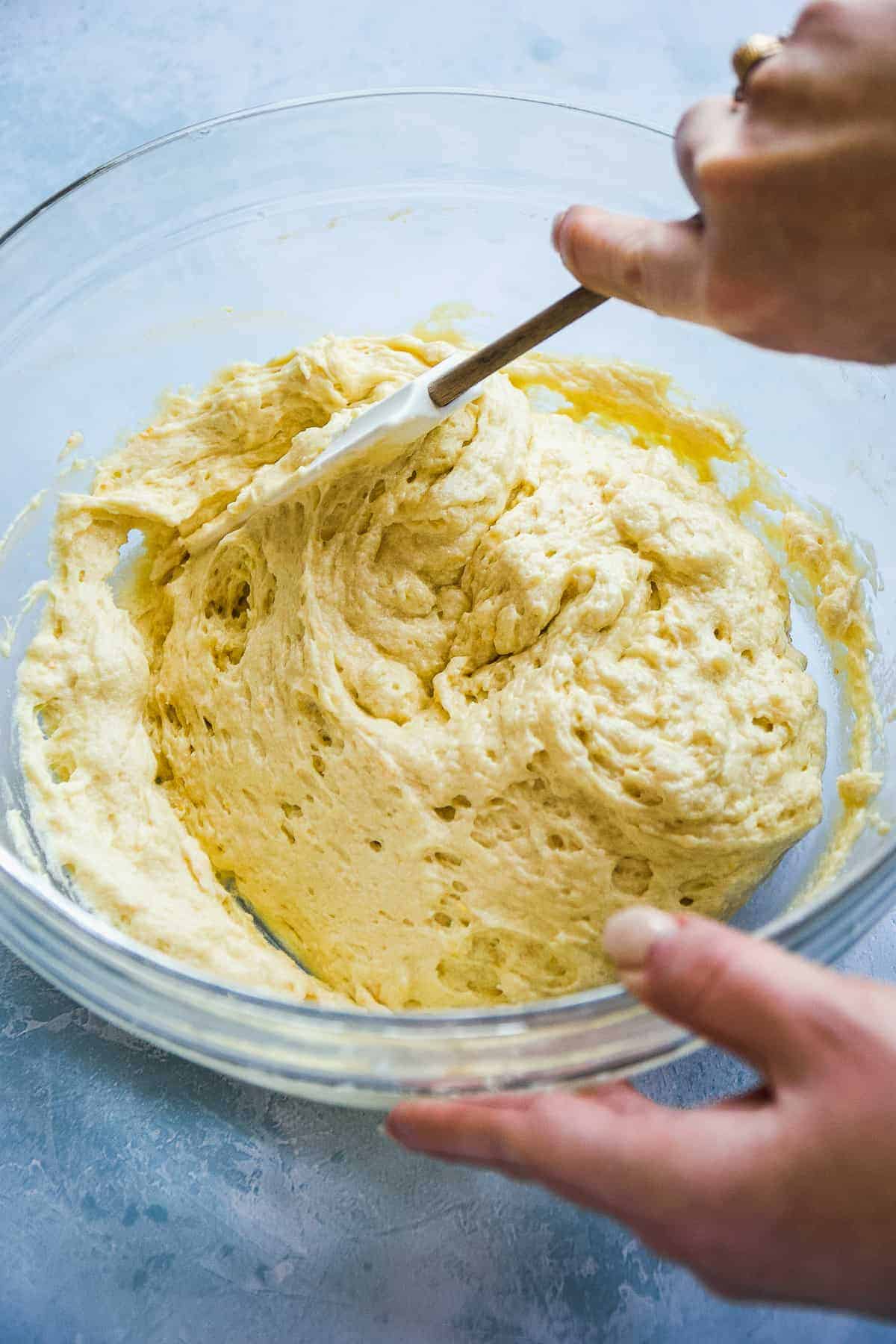 Person mixing orange pound cake batter in a clear bowl.