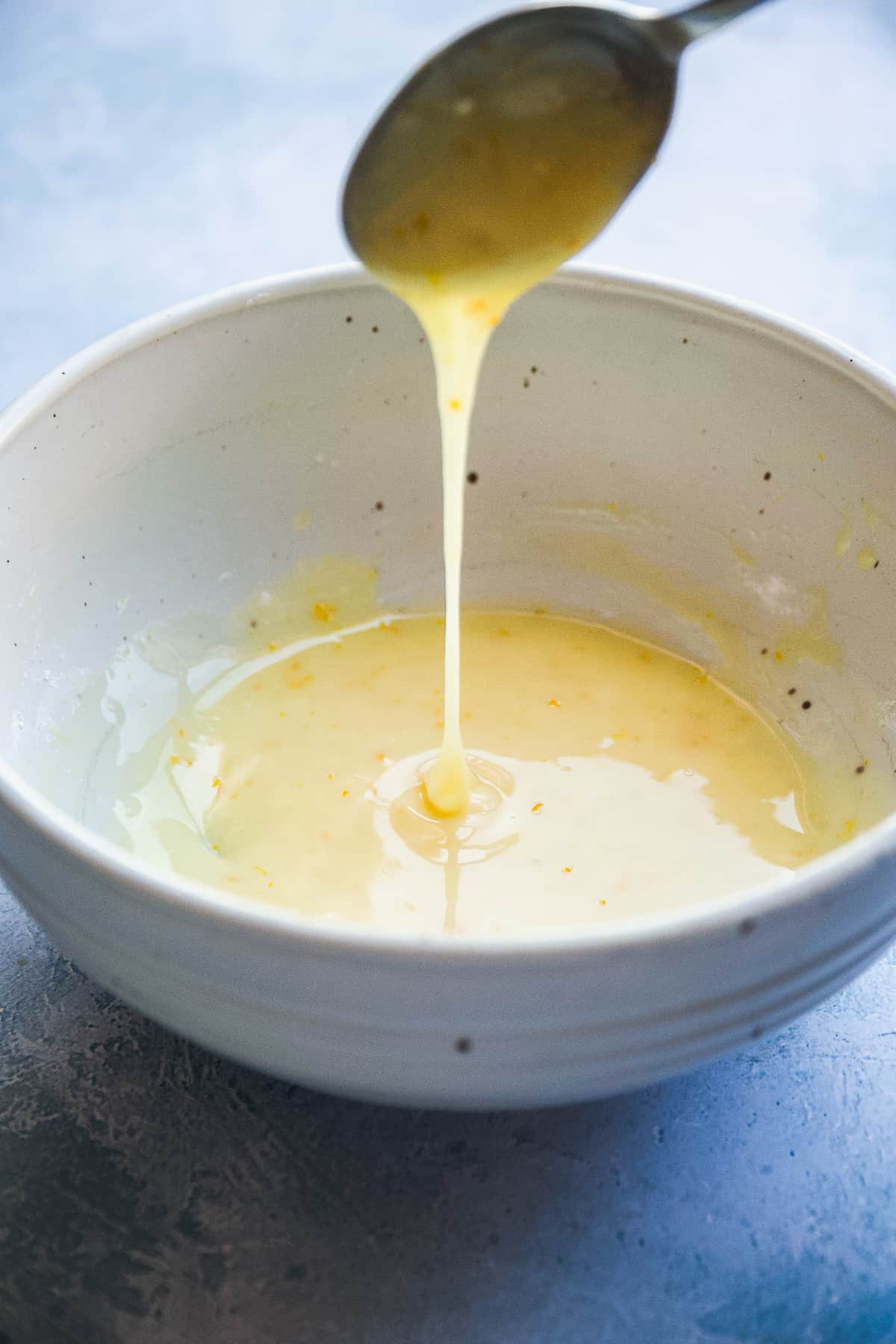 Gray bowl with orange glaze being mixed and dripping off a spoon.