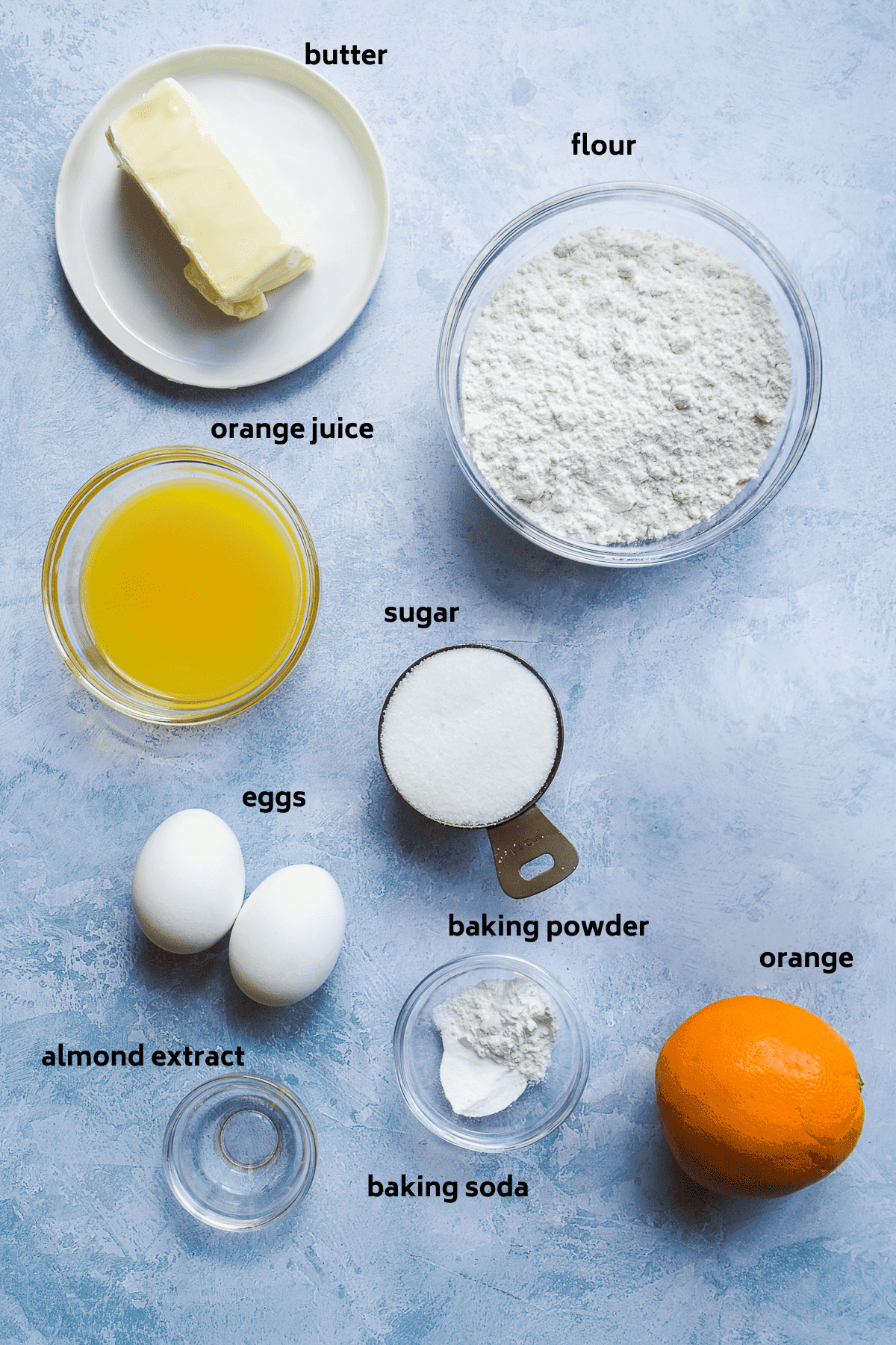 Orange pound cake ingredients on a blue surface with labels in black.