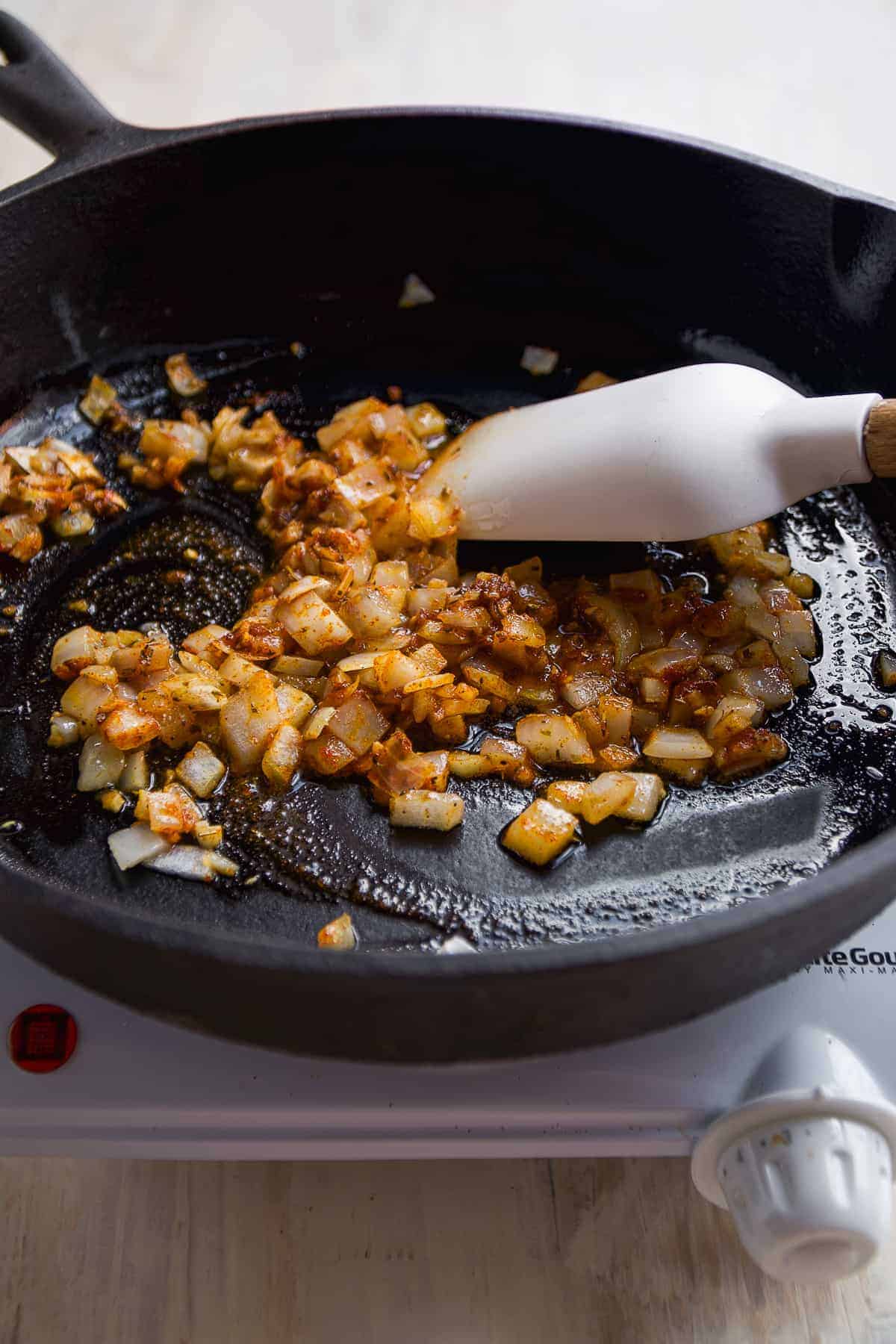 Diced white onion being cooked in a black skillet.