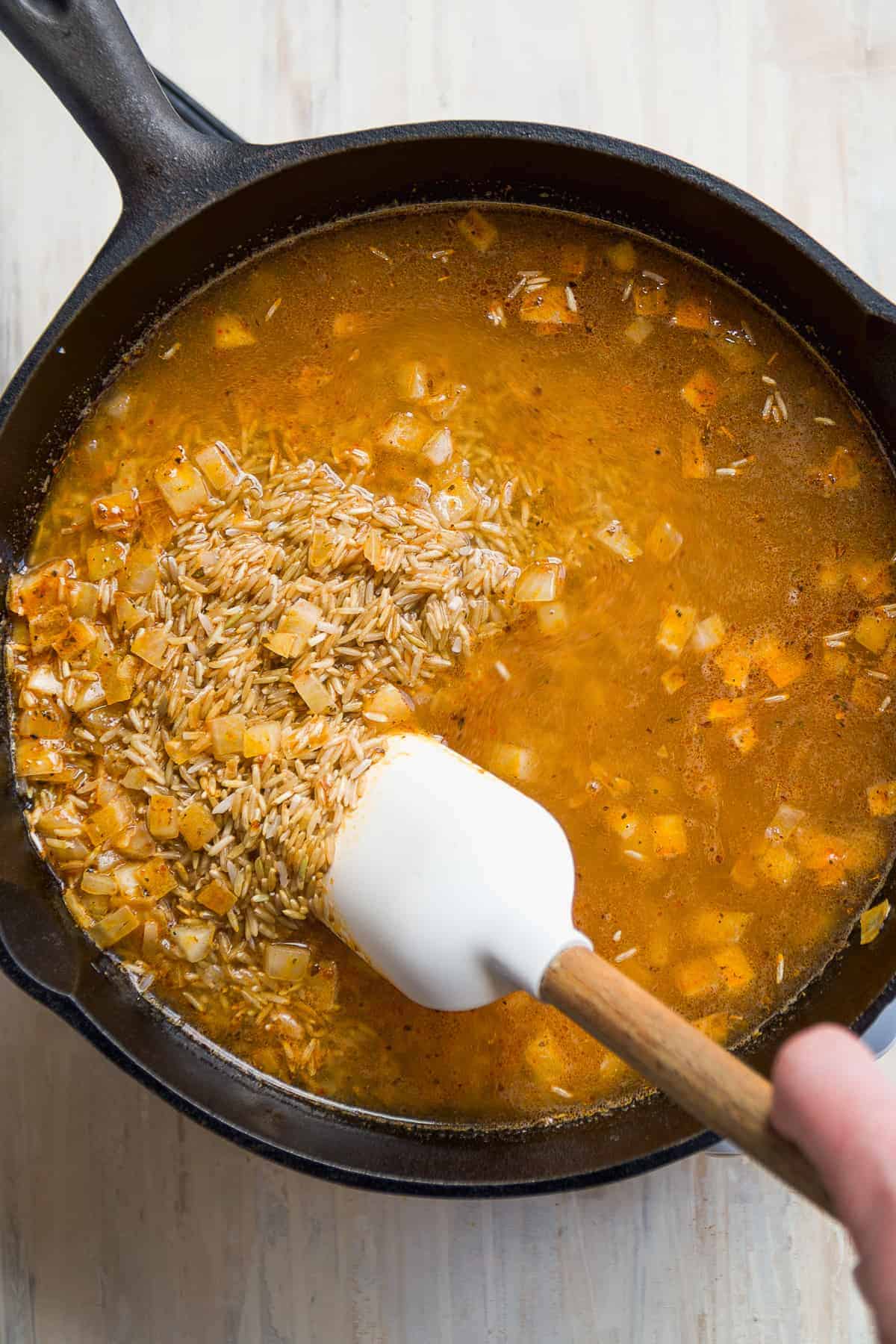 Person mixing rice and broth into the skillet.