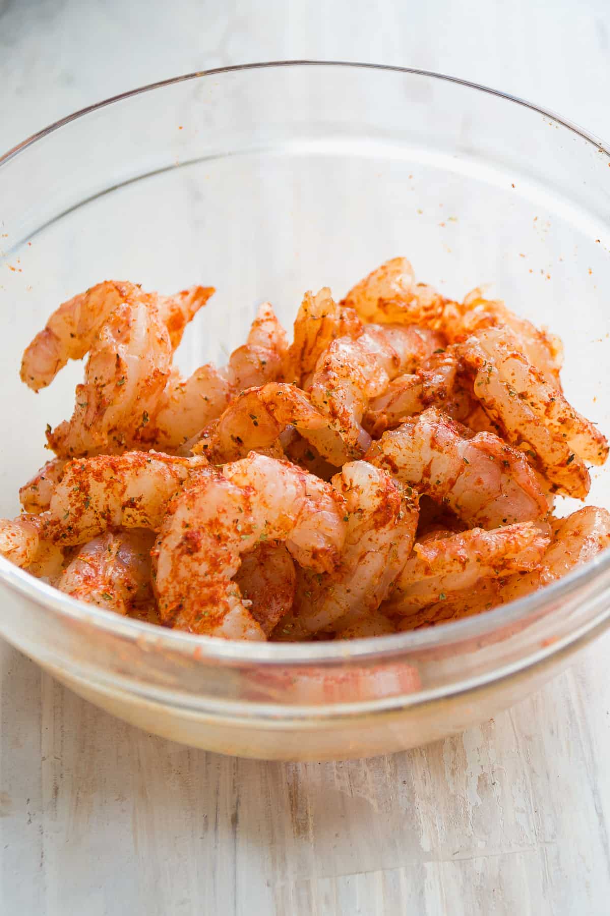 Shrimp tossed in a clear mixing bowl with seasonings.