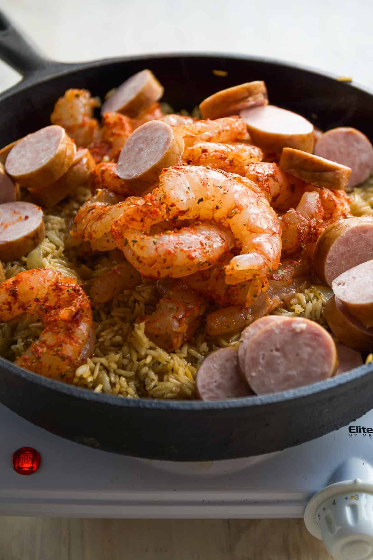 Shrimp and kielbasa about to be cooked in a black skillet.