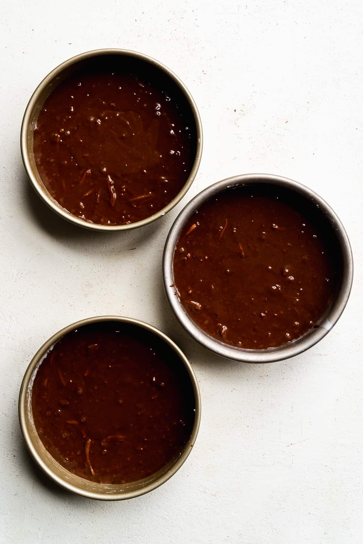 Three cake pans with chocolate cake batter about be be baked.