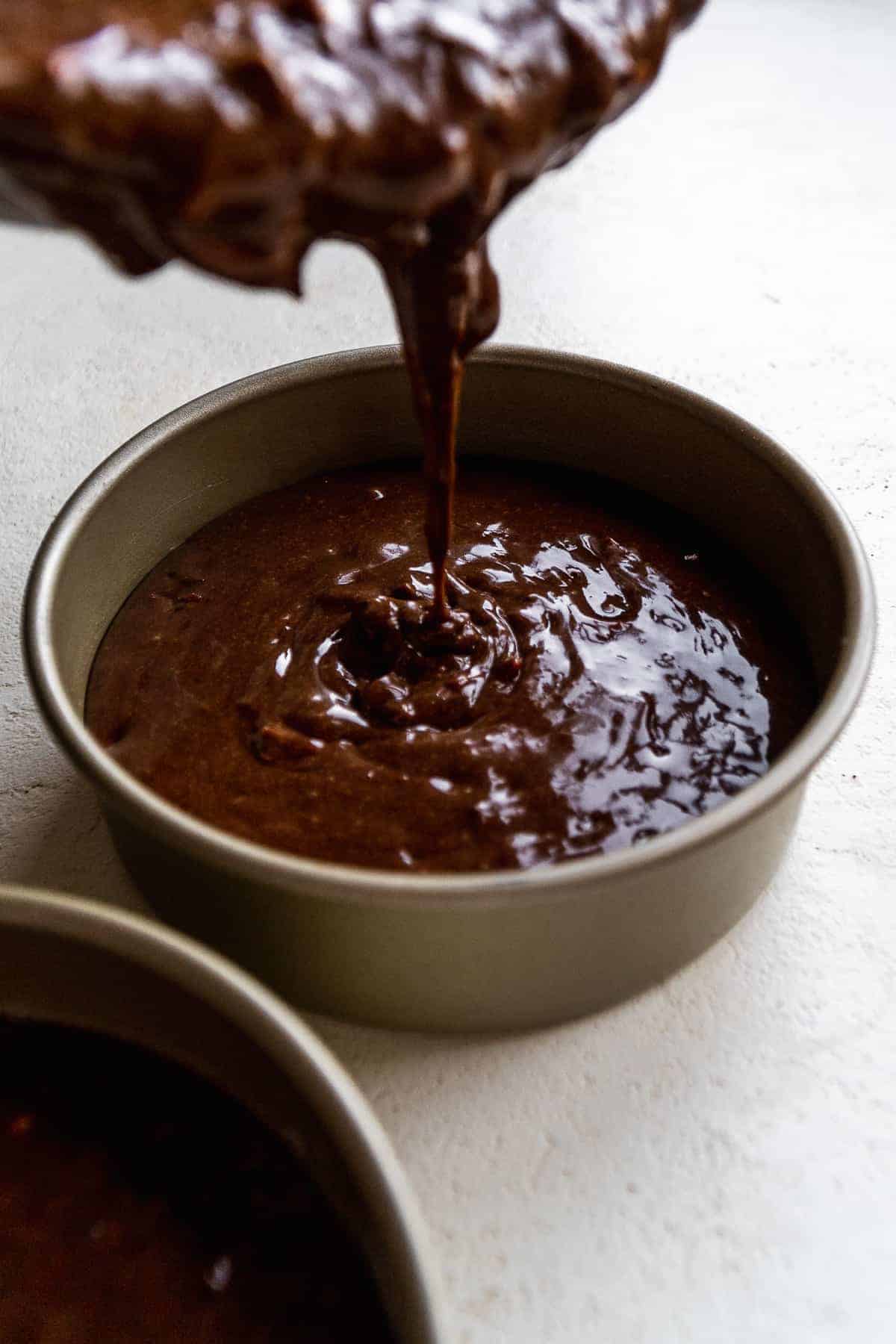 Chocolate cake batter being poured into a silver cake pan.