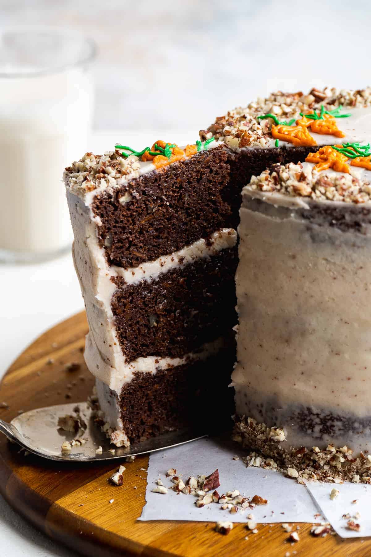 A slice of chocolate carrot cake being removed from a cake on a wooden platter.