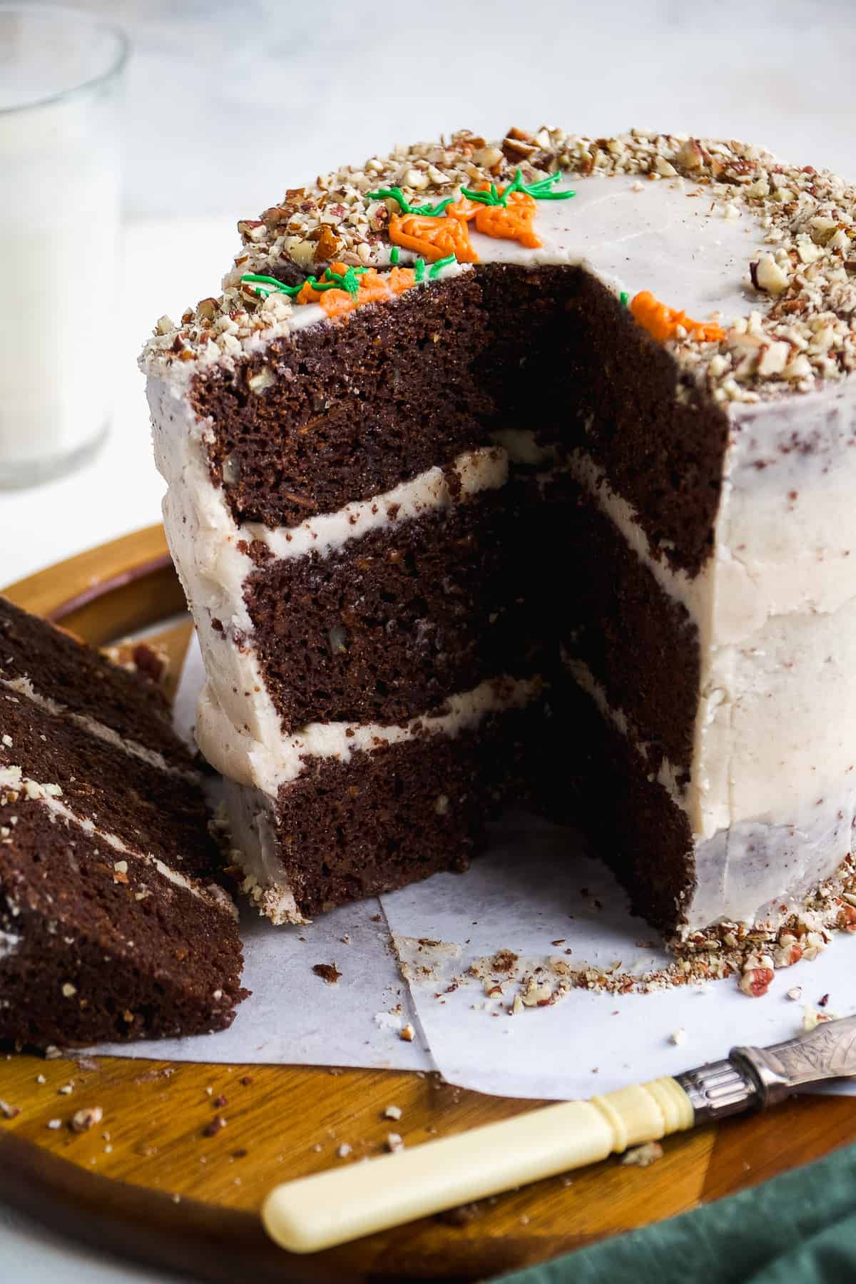 Chocolate carrot cake with a few slices cut out on a wooden platter.