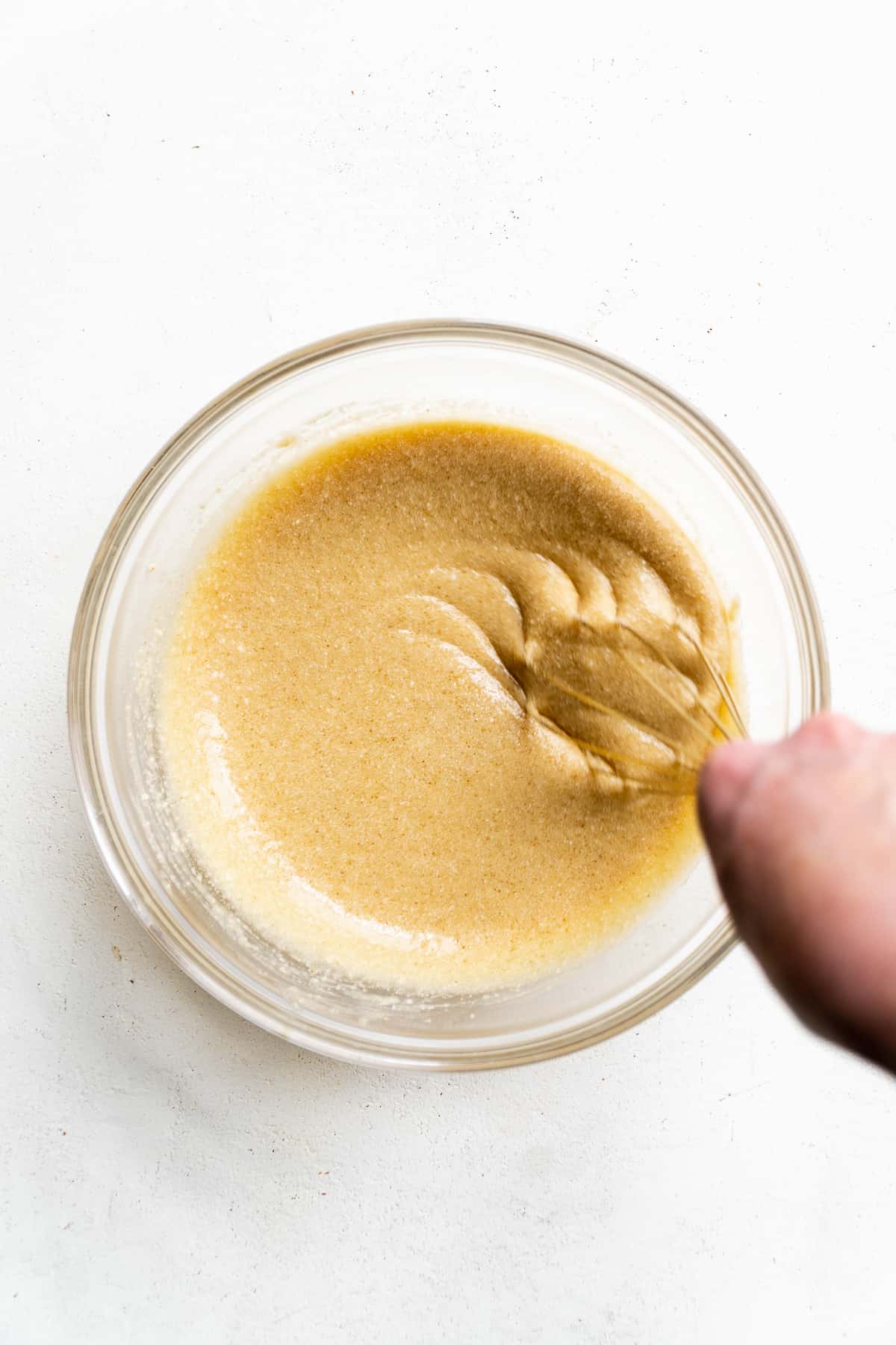 Person mixing wet cake ingredients together with a whisk.