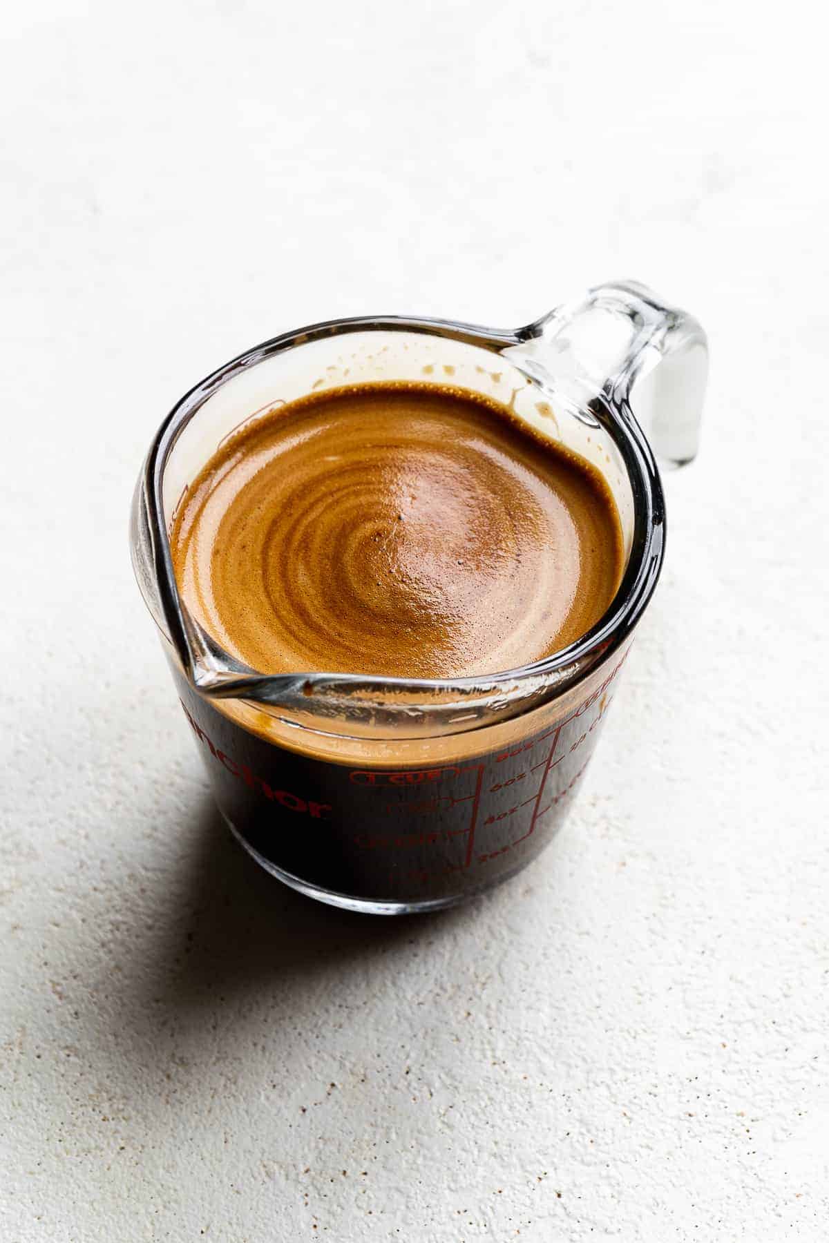 Espresso in a measuring cup on a white surface.