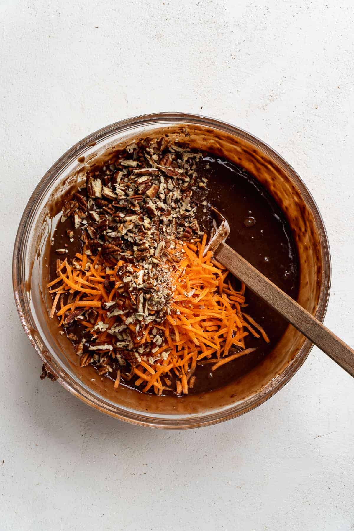 Overhead view of a mixing bowl with chocolate cake batter and carrots and pecans about to be mixed in.