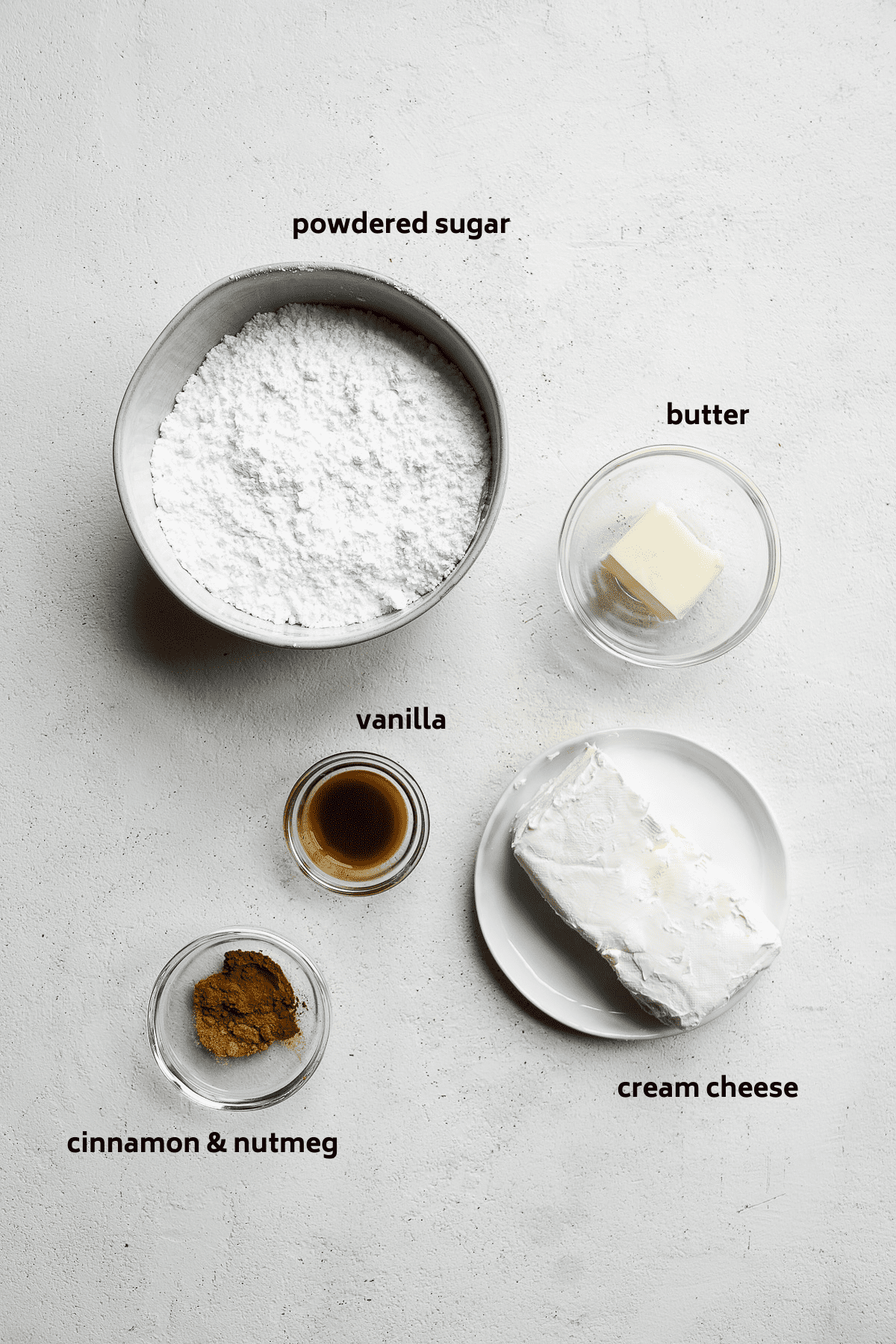 Cream cheese icing ingredients on a white surface with labels in black.