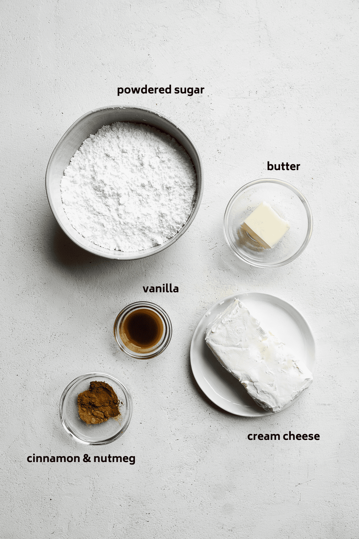 Cream cheese icing ingredients on a white surface with labels in black.